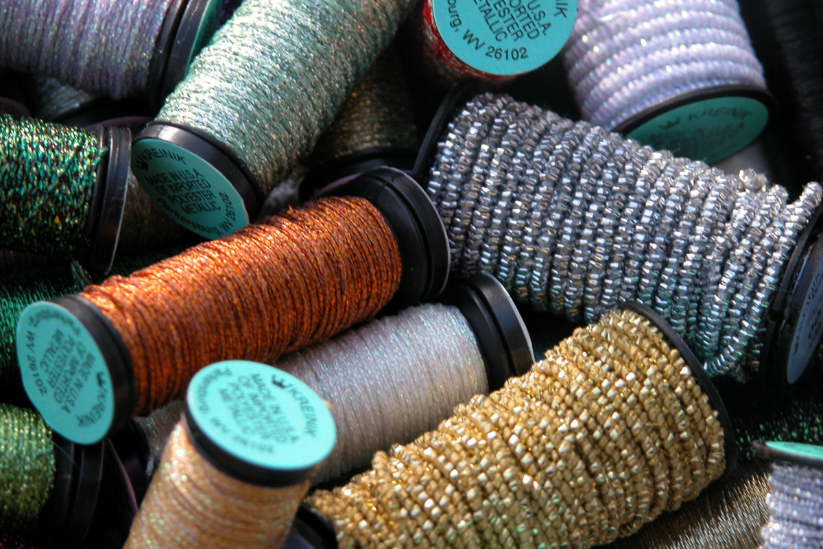 A pile of different colours and types of Kreinik cross stitching thread, still on the spool