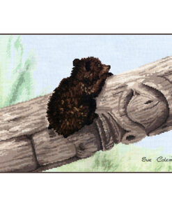 A tiny Brown Bear cub clings to the side of a fallen tree, which is carved into a half-completed totem pole